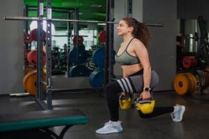 Young fit woman doing lunges exercise with kettlebells in the gym. Free weights, functional training